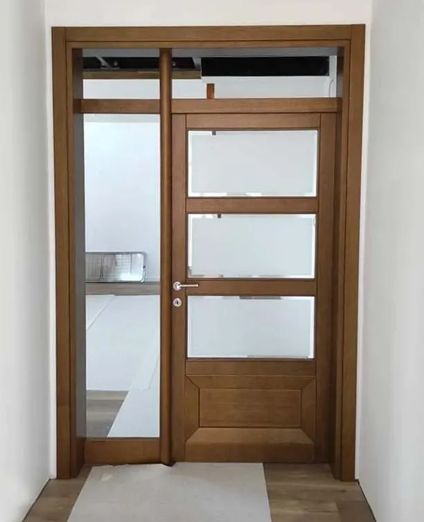 Light walnut-tone solid wood door with three frosted panes, clear side light and transom, on site