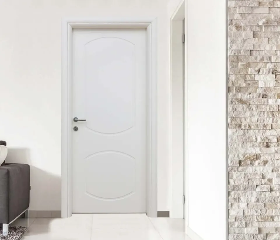 White door with two arched panels beside a grey sofa and a stone wall